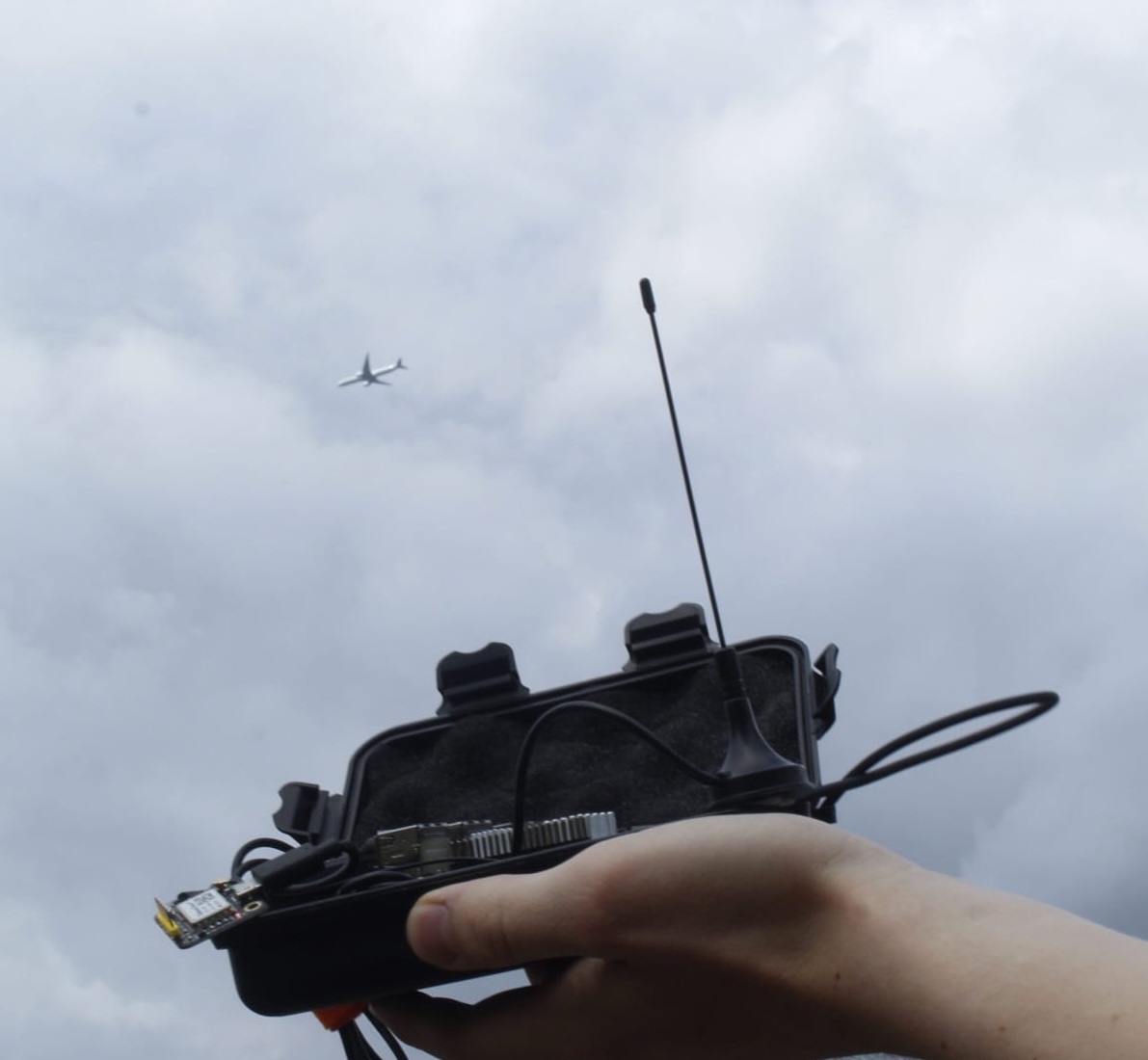 A small pelican case with a raspberry pi and an antenna held up in front of a passing aircraft